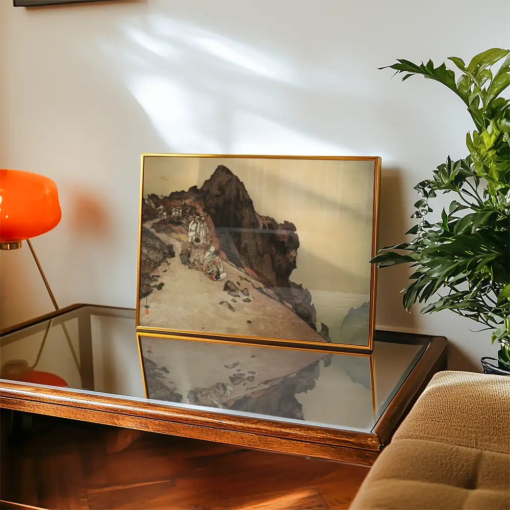 Framed painting of a rocky landscape displayed on a wooden table with a modern orange lamp and a green plant in the background.