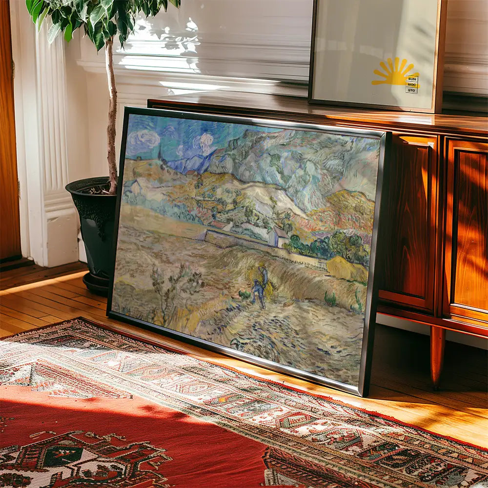 Framed painting leaning against a wooden cabinet in a cozy room, featuring a landscape scene with rolling hills and a figure working the land, surrounded by indoor plants and a patterned rug.