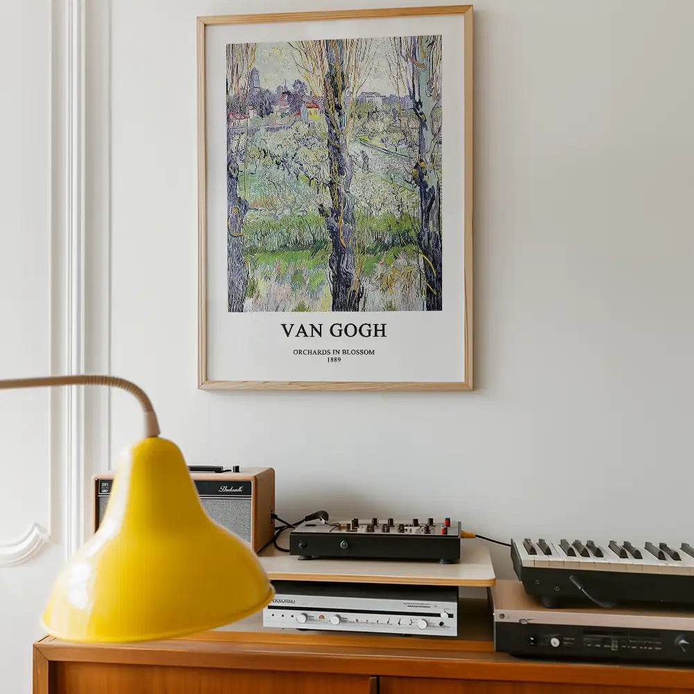 Framed poster of Vincent Van Gogh's painting "Orchards in Blossom" from 1889, displayed on a wall above a wooden shelf with a yellow lamp and vintage audio equipment.