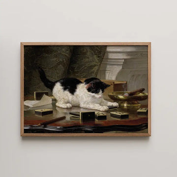 A framed painting of a black and white cat playing on a wooden table surrounded by small objects and a bowl.
