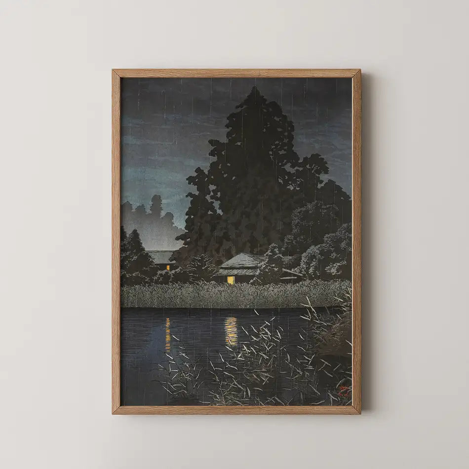 Framed painting of a serene night scene featuring a dark silhouette of trees and a house by a calm water body reflecting dim yellow lights.