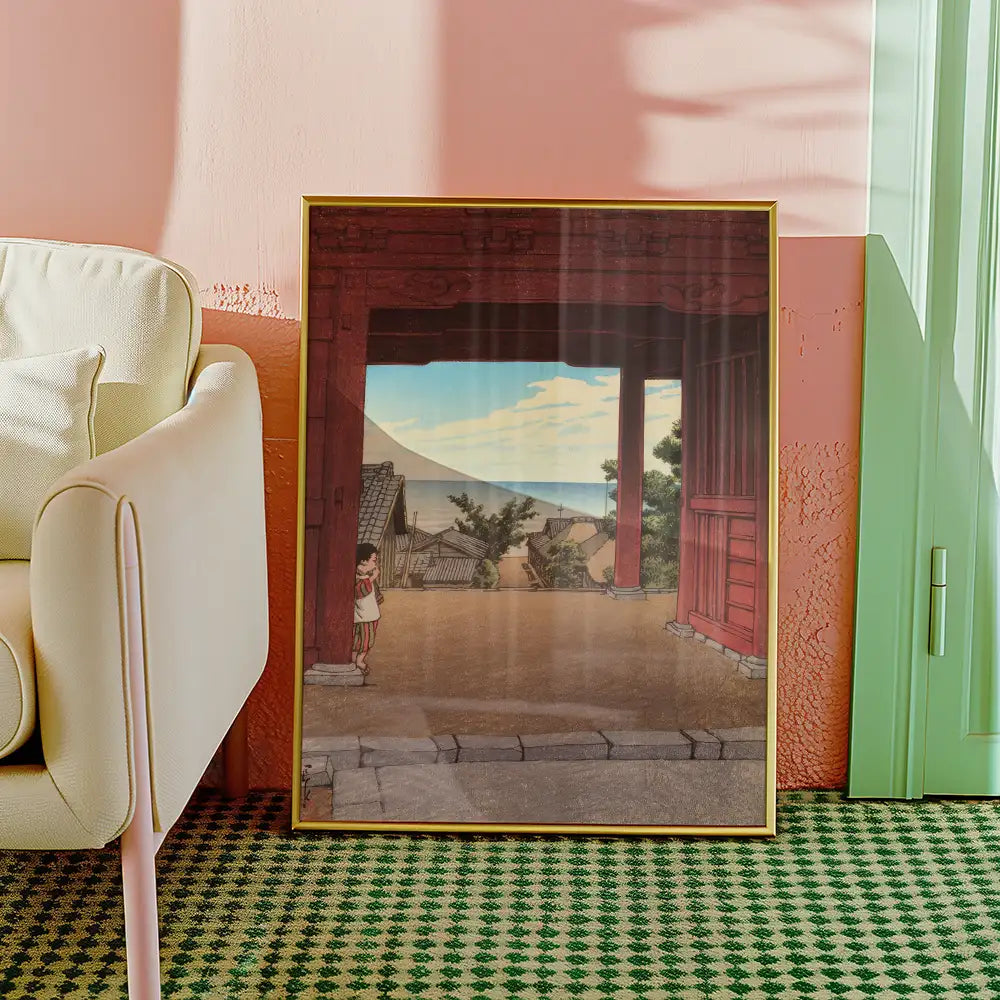Framed painting of a serene landscape with traditional architecture and a child standing at the entrance, set in a cozy living room with a light-colored armchair and pastel-colored walls.