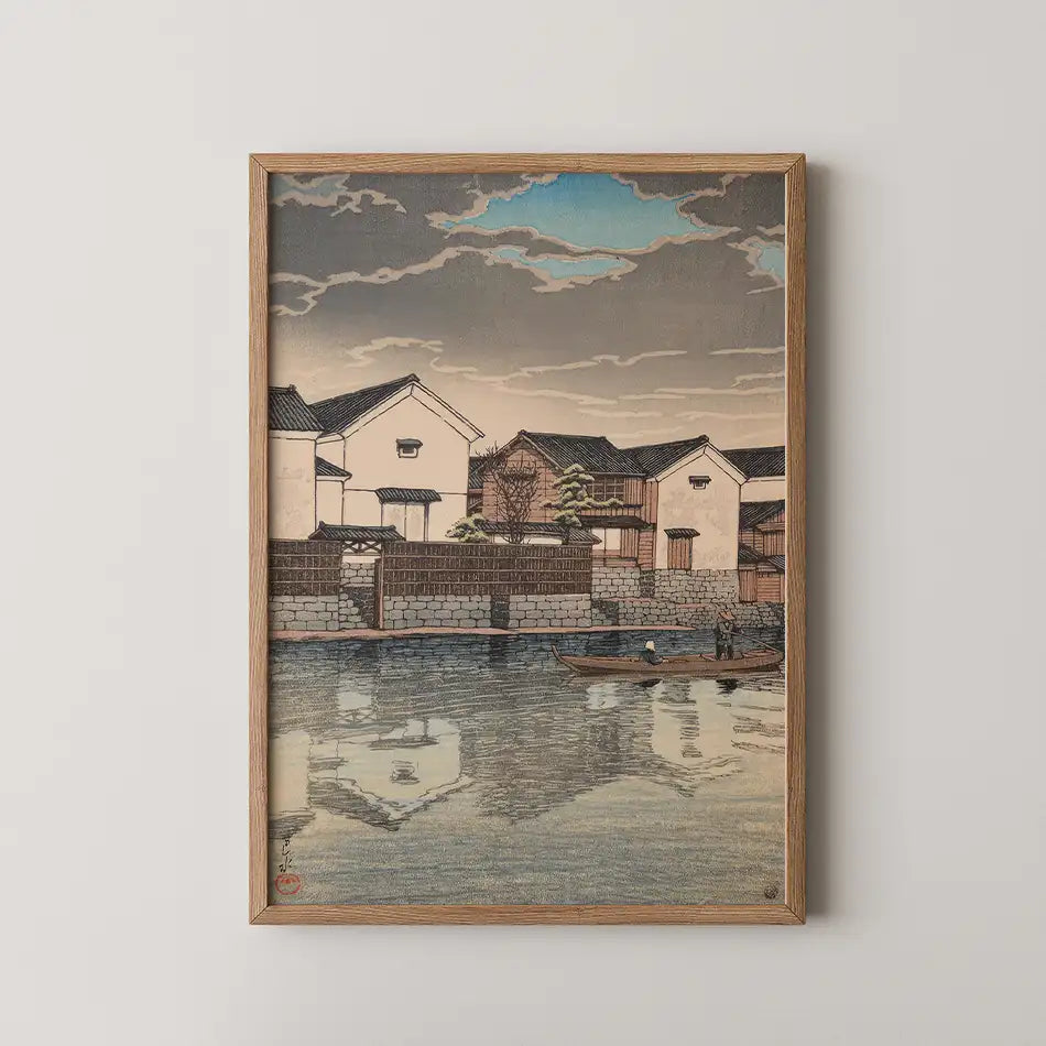 Framed painting of traditional waterfront houses and a boat on water, featuring a cloudy sky and serene reflection.