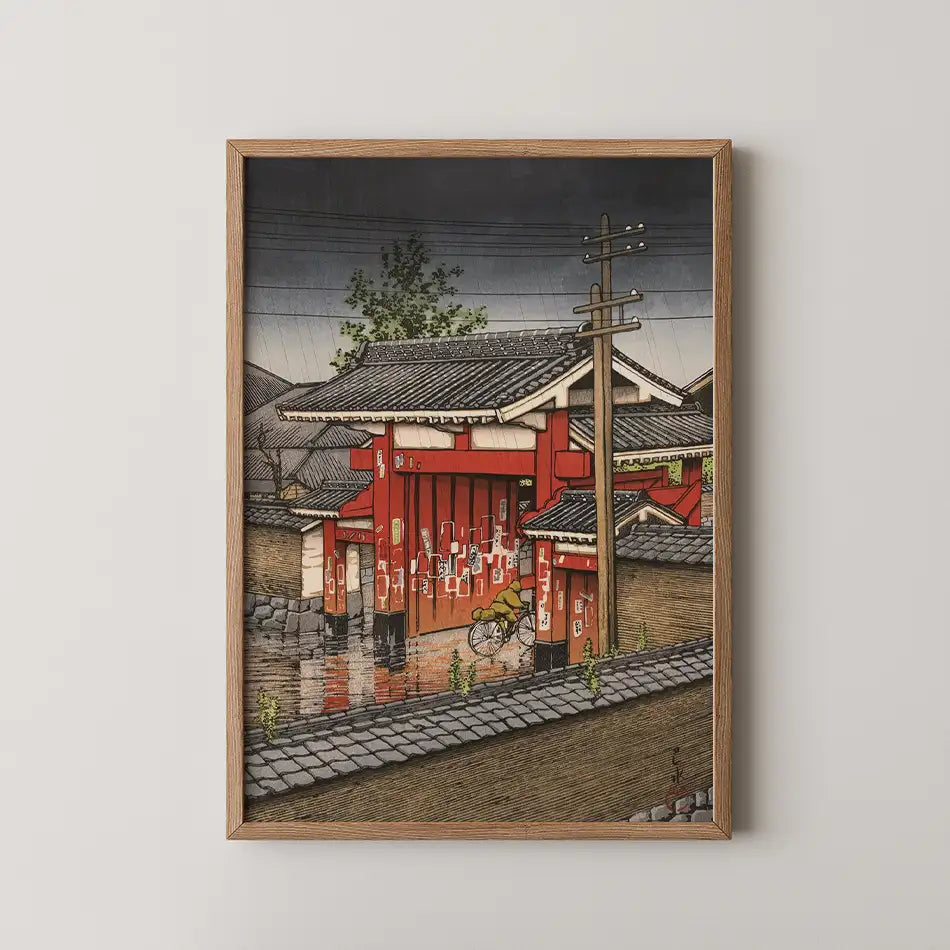 Japanese-inspired painting of a red building with a bicycle, framed in wood, depicting a rainy scene with muted colors and traditional architecture.