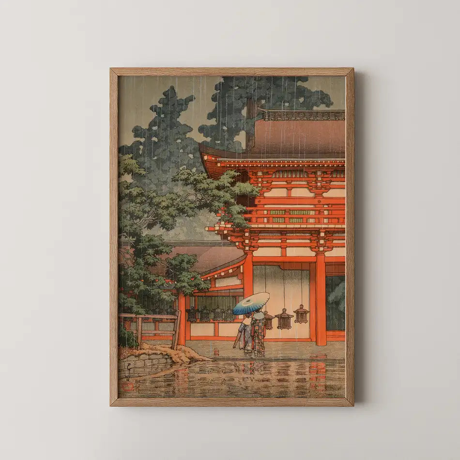 Painting of a traditional Japanese scene featuring a wooden temple and two figures with an umbrella, framed in light wood.