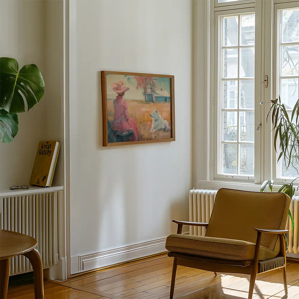 A framed painting of a woman in a pink dress and hat sitting in a field with a dog, displayed in a bright living room with a chair and potted plant.