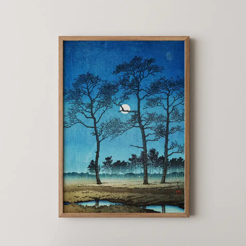 Painting of silhouetted trees against a deep blue night sky with a full moon and a tranquil landscape below, presented in a wooden frame.