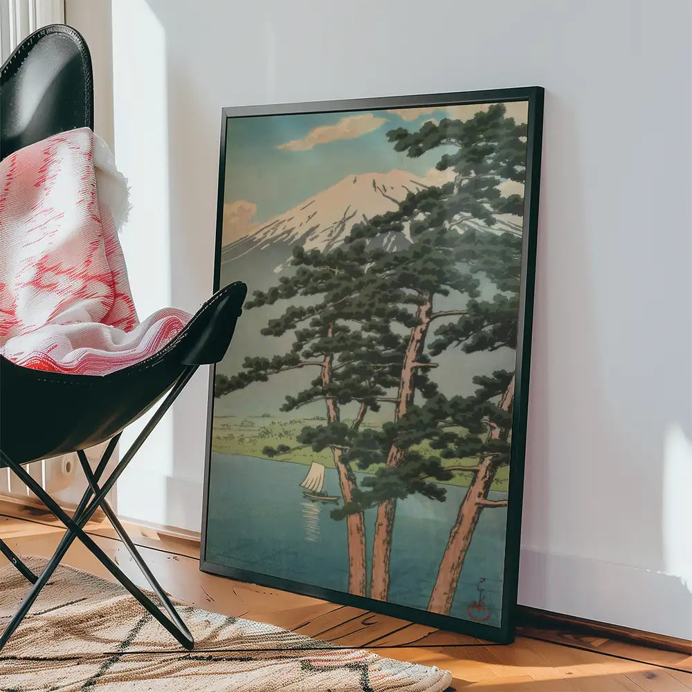 Framed painting of a serene landscape featuring pine trees, a lake, and a mountain in the background, leaning against a black chair with a cozy throw blanket.