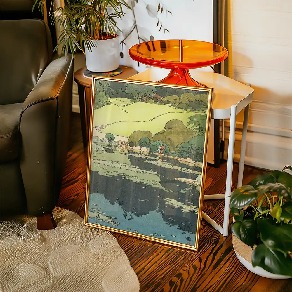Framed landscape painting featuring rolling green hills and a serene water scene, displayed in a cozy living room setting.
