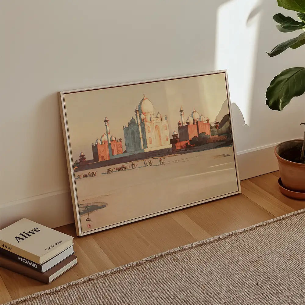 A framed painting of the Taj Mahal displayed against a wall with a potted plant and books in the foreground.