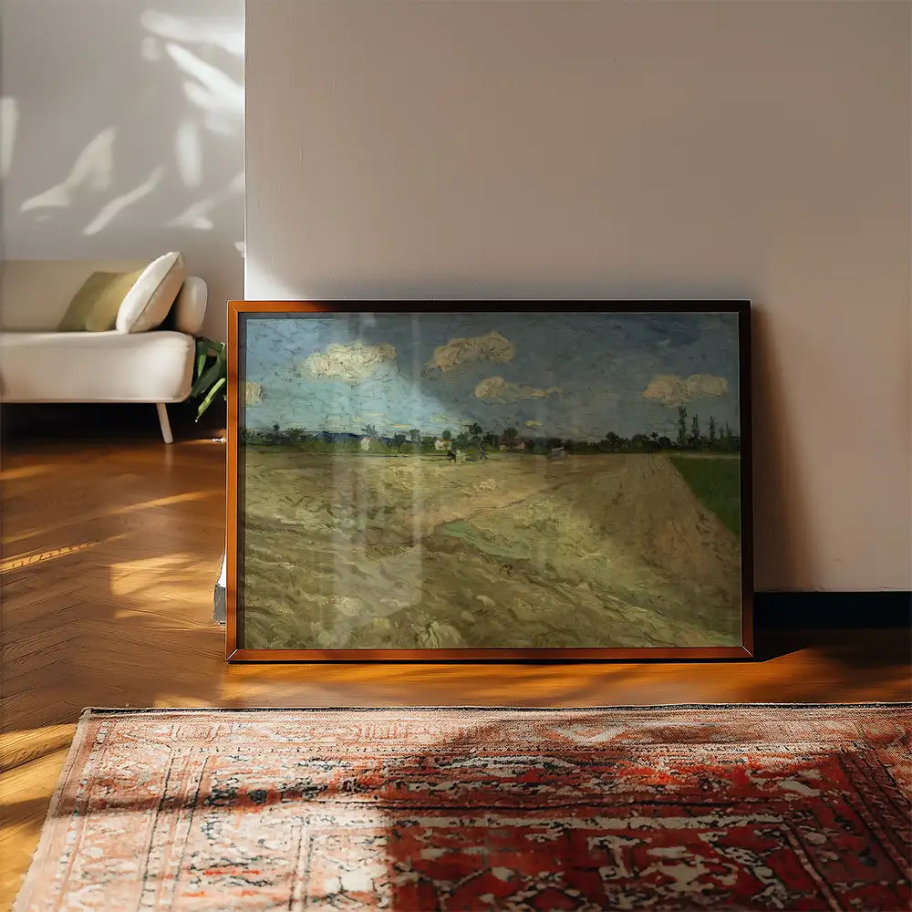 Framed painting of a landscape with fields and clouds, resting against a wall in a sunlit room with wooden flooring and a patterned rug.