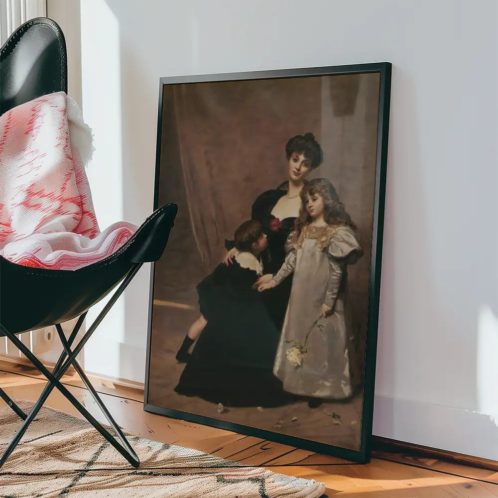 Framed vintage painting of a woman with two children, displayed beside a black chair with a blanket on a wooden floor.