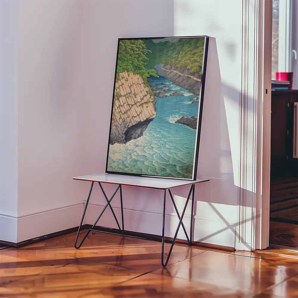 Framed painting of a serene coastal landscape with turquoise waters and rocky cliffs, displayed on a minimalist table in a bright interior setting.
