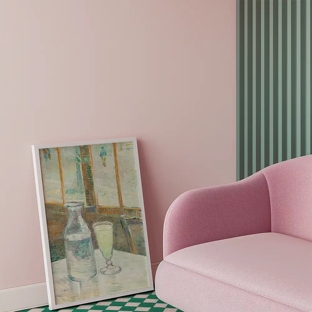 A painting of a glass of green beverage and a water pitcher displayed against a pink wall beside a pink sofa