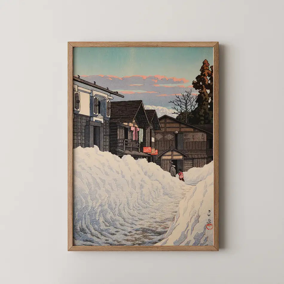 Framed painting depicting a snow-covered street with traditional wooden houses and a sunset sky.