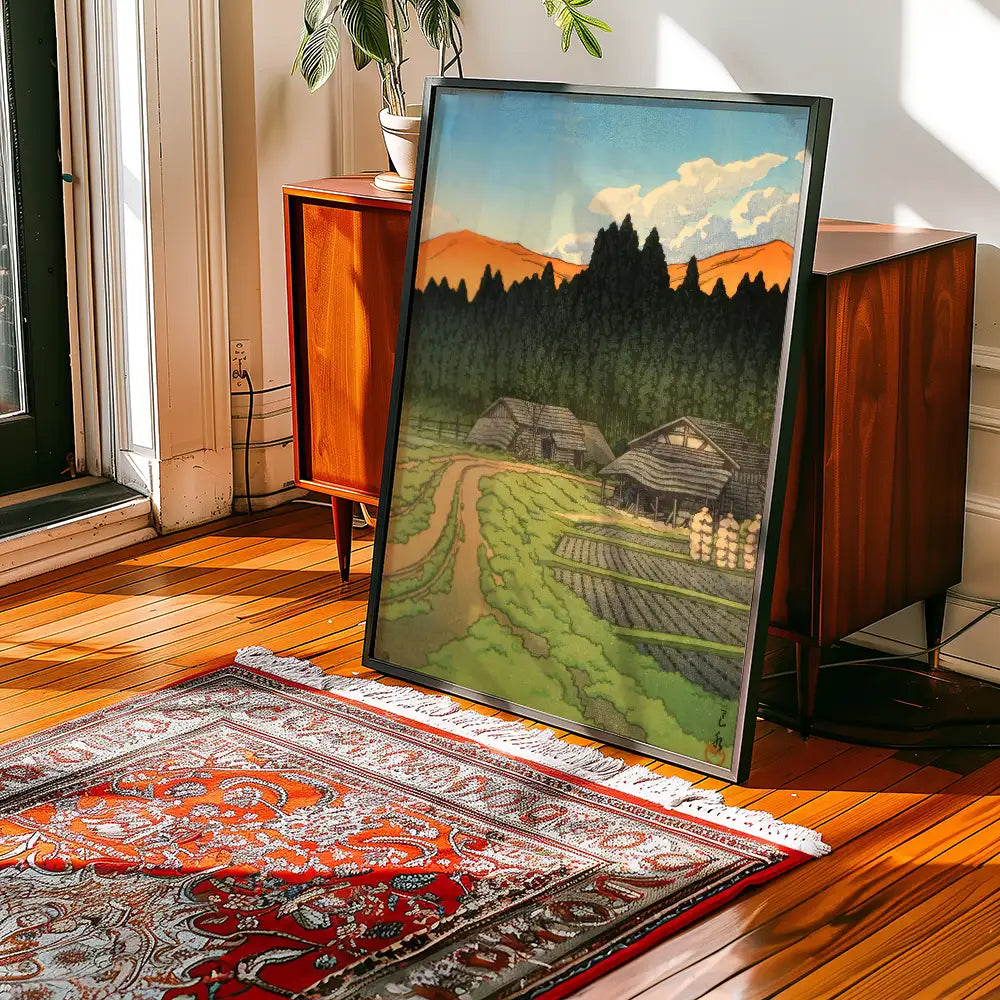 Framed landscape painting depicting a rural scene with mountains and fields in a bright, sunlit room setting.