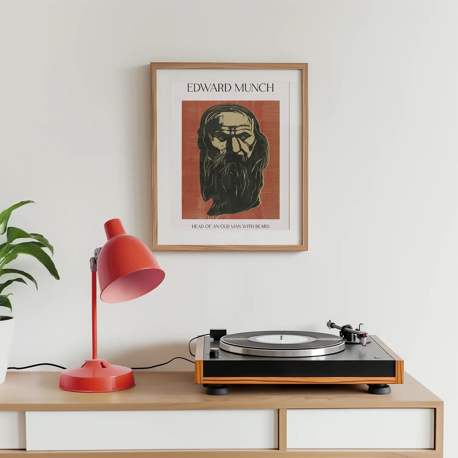 Framed painting titled "Head of an Old Man with Beard" by Edward Munch displayed on a wall above a wooden table with a record player and a red desk lamp.