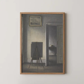 Framed painting depicting a shadowy interior scene with an empty easel and a table, featuring muted colors and soft lighting.