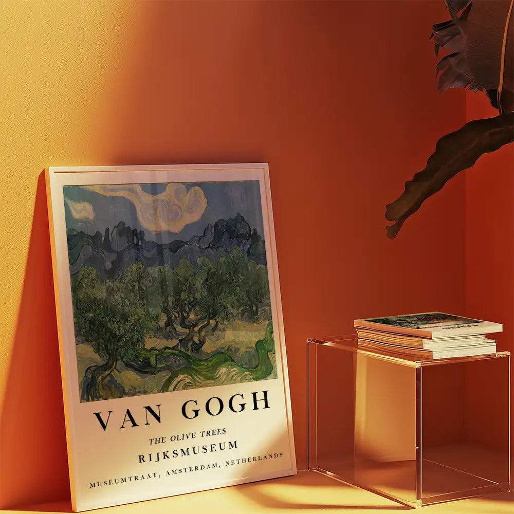 Van Gogh painting poster titled "The Olive Trees" displayed against an orange wall, accompanied by a stack of books on a clear table.
