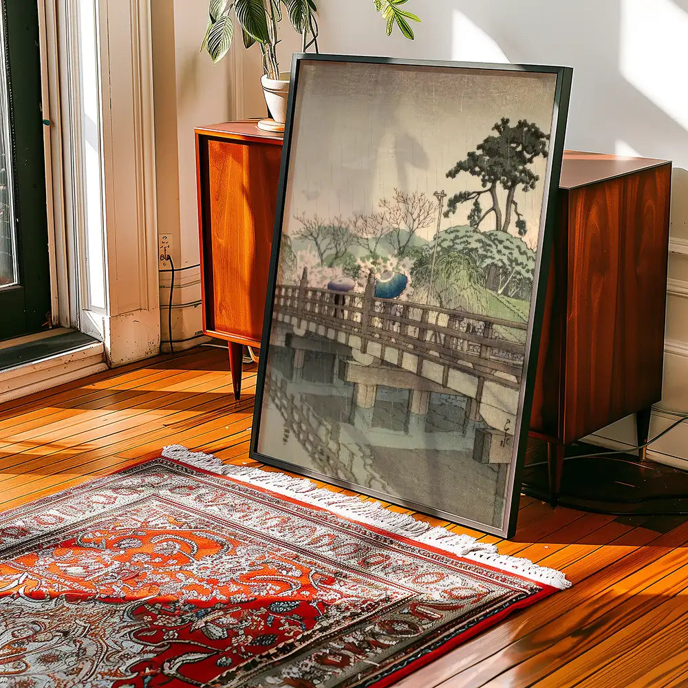 Framed painting of a serene landscape with a bridge and trees, leaning against a wooden cabinet on a wooden floor with a decorative rug.