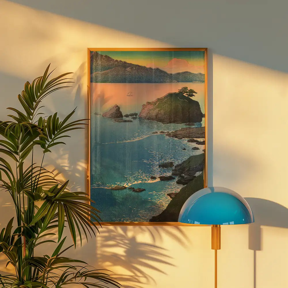 Framed landscape painting of a coastal scene with rocky islands and a sunset, displayed on a wall beside a green plant and a blue lamp.
