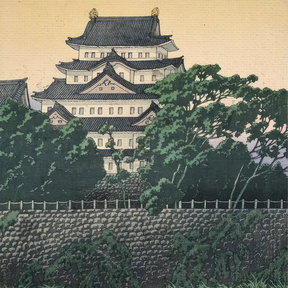 Historic Japanese castle surrounded by lush greenery and a stone wall at sunset.