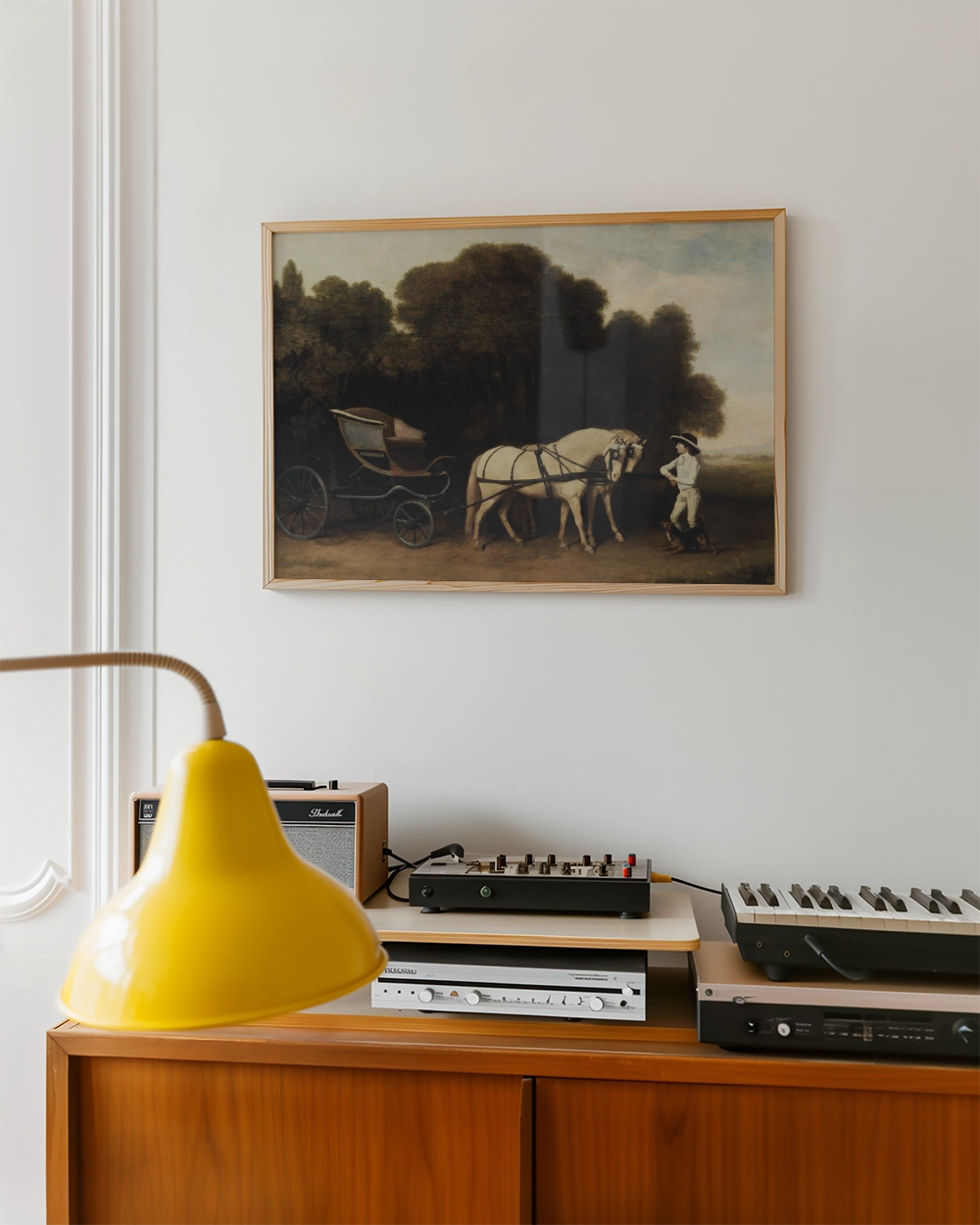 Painting of a horse-drawn cart in a landscape, framed above a wooden cabinet with a yellow lamp and audio equipment.