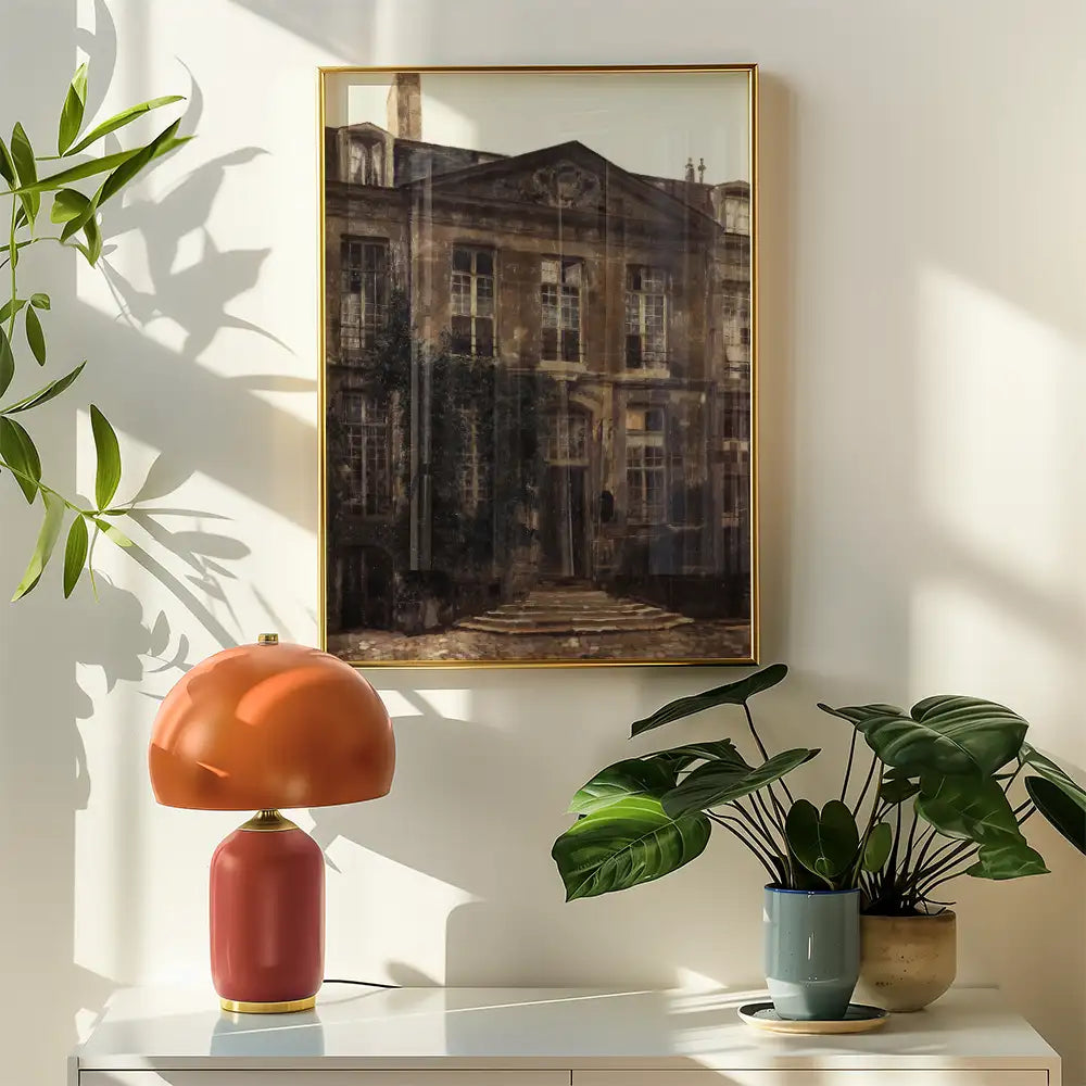 Framed painting of a building with an overgrown entrance, displayed on a wall next to a modern lamp and potted plants.