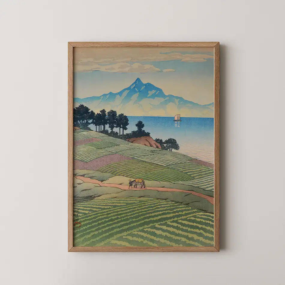 Framed painting of rolling green hills with a horse-drawn cart, mountain backdrop, and a ship on the water under a blue sky with clouds.