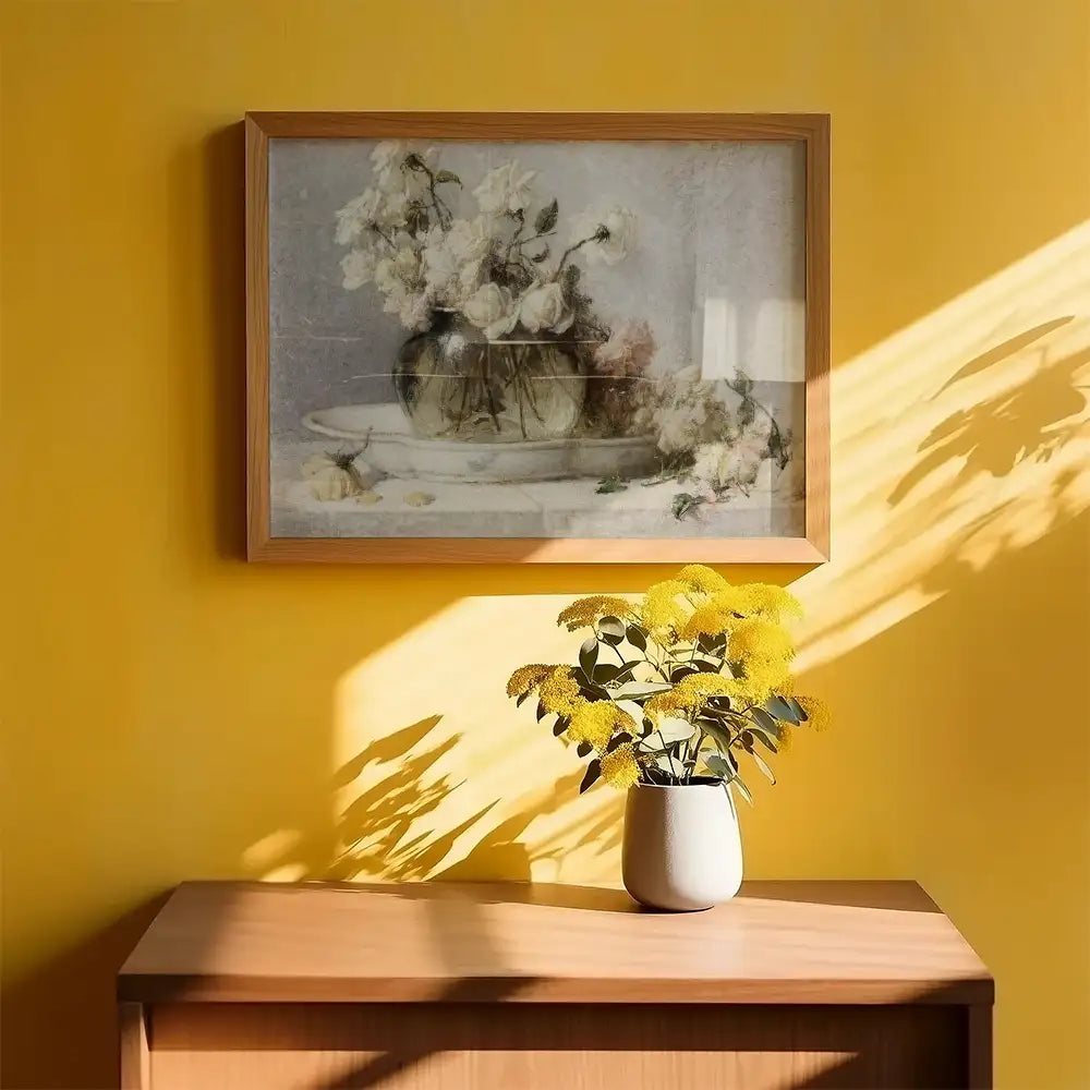 Framed painting of a floral arrangement in a vase, displayed on a bright yellow wall alongside a vase of yellow flowers on a wooden table.
