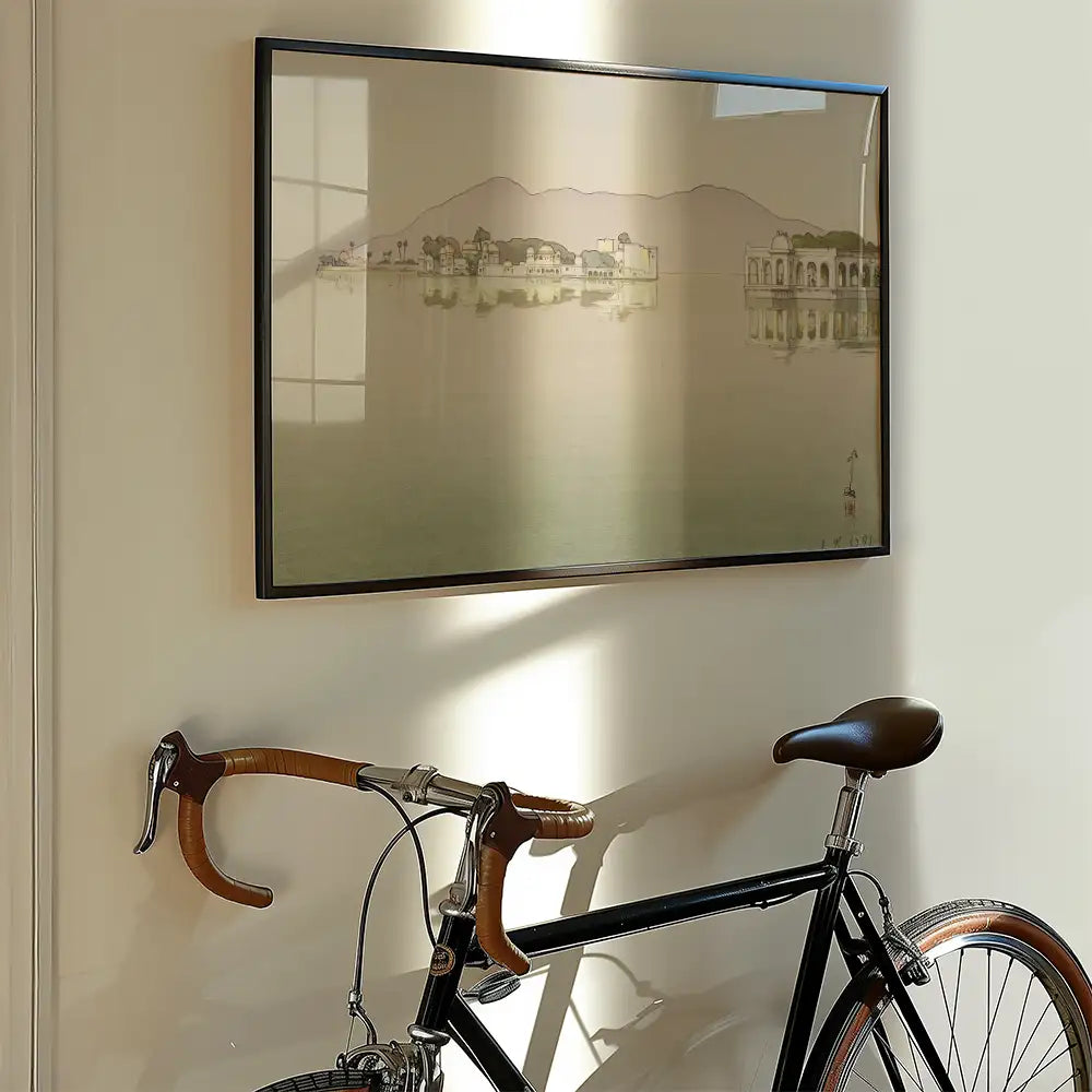 Framed painting of a serene landscape with mountains and buildings, displayed on a wall next to a black bicycle with brown details.