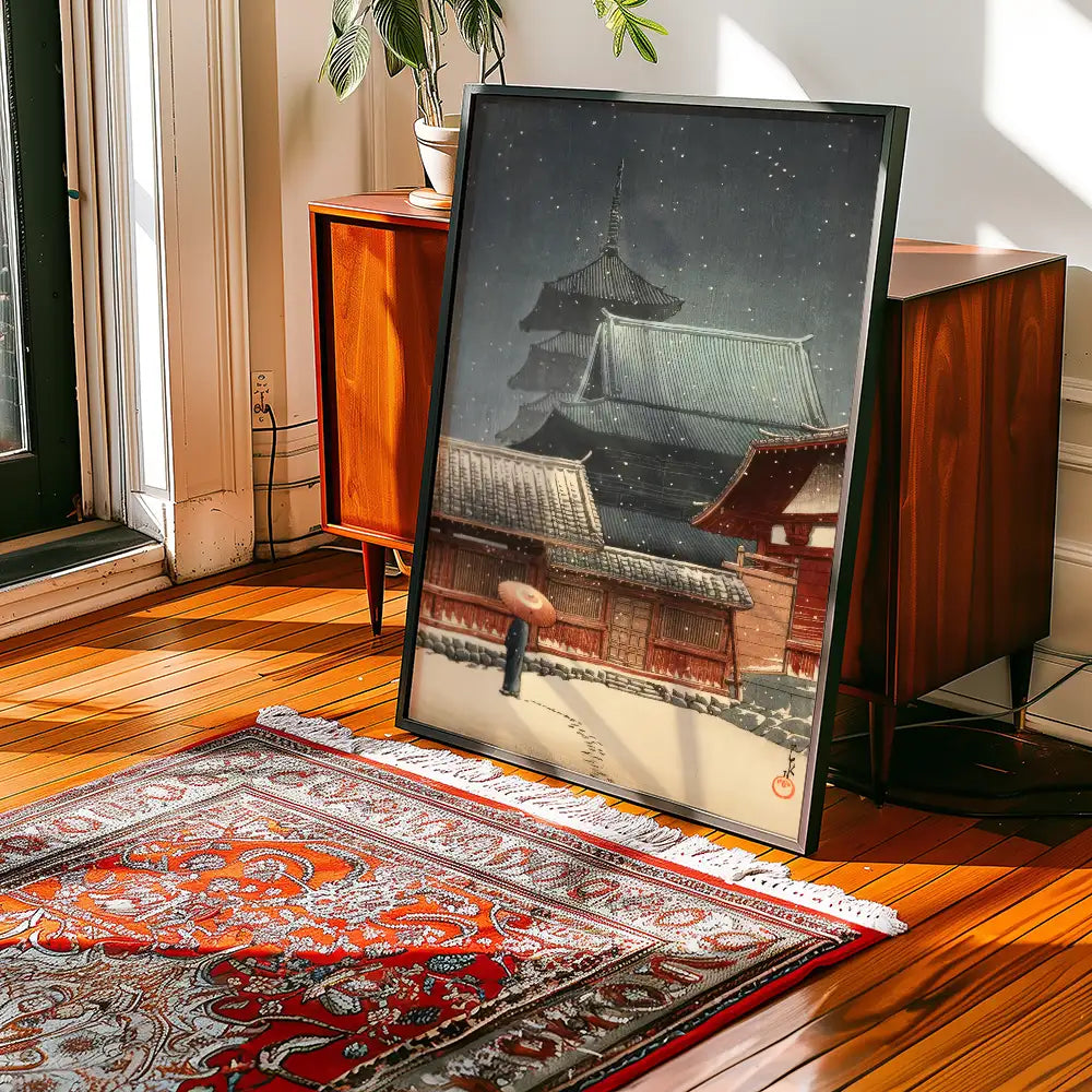 Framed painting of a traditional Japanese temple in the snow, placed next to a wooden cabinet on a vibrant area rug.