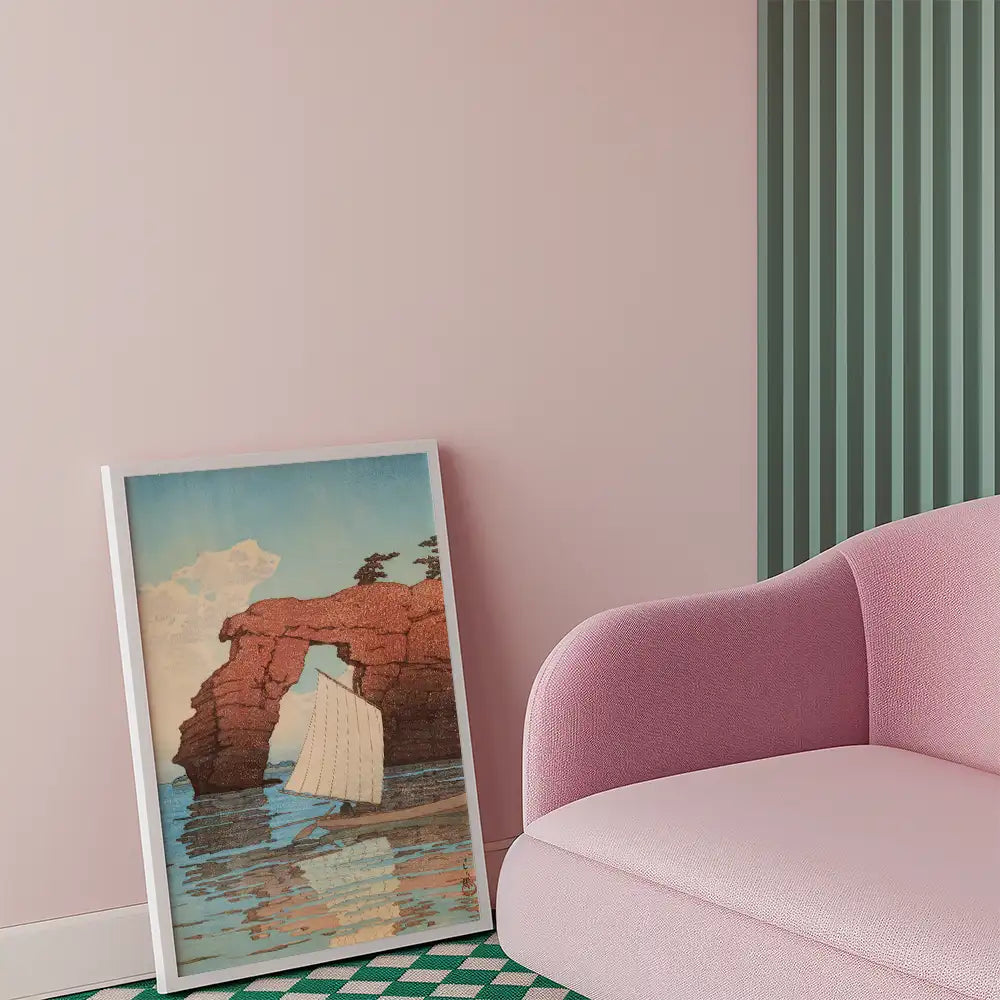Painting of a sailboat near a rock formation with a blue sky and clouds, displayed next to a pink sofa in a stylish interior.