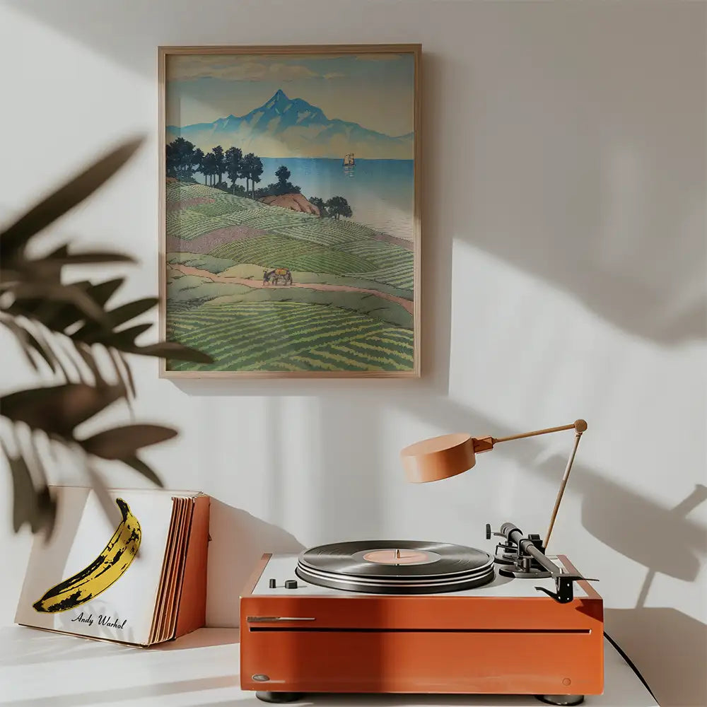 Framed landscape painting featuring rolling hills and a mountain backdrop, displayed above a modern record player and vinyl collection in a stylish interior setting.