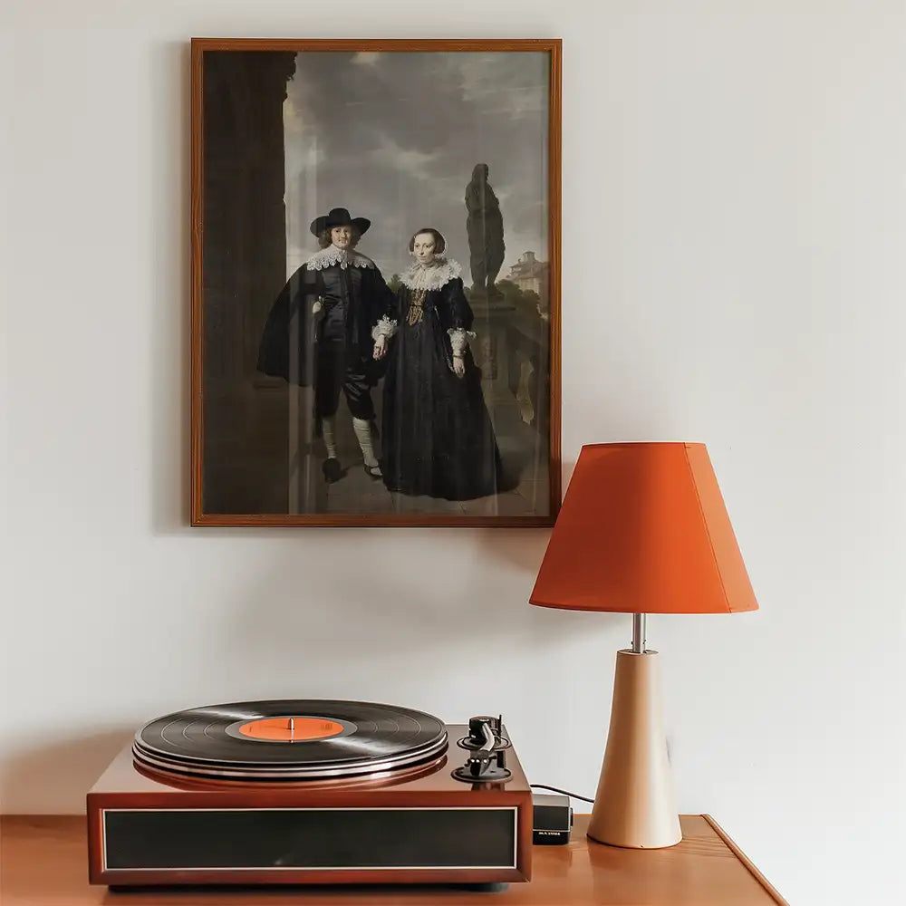 Framed painting of a couple in historical attire hanging above a vintage record player and a modern orange lamp.