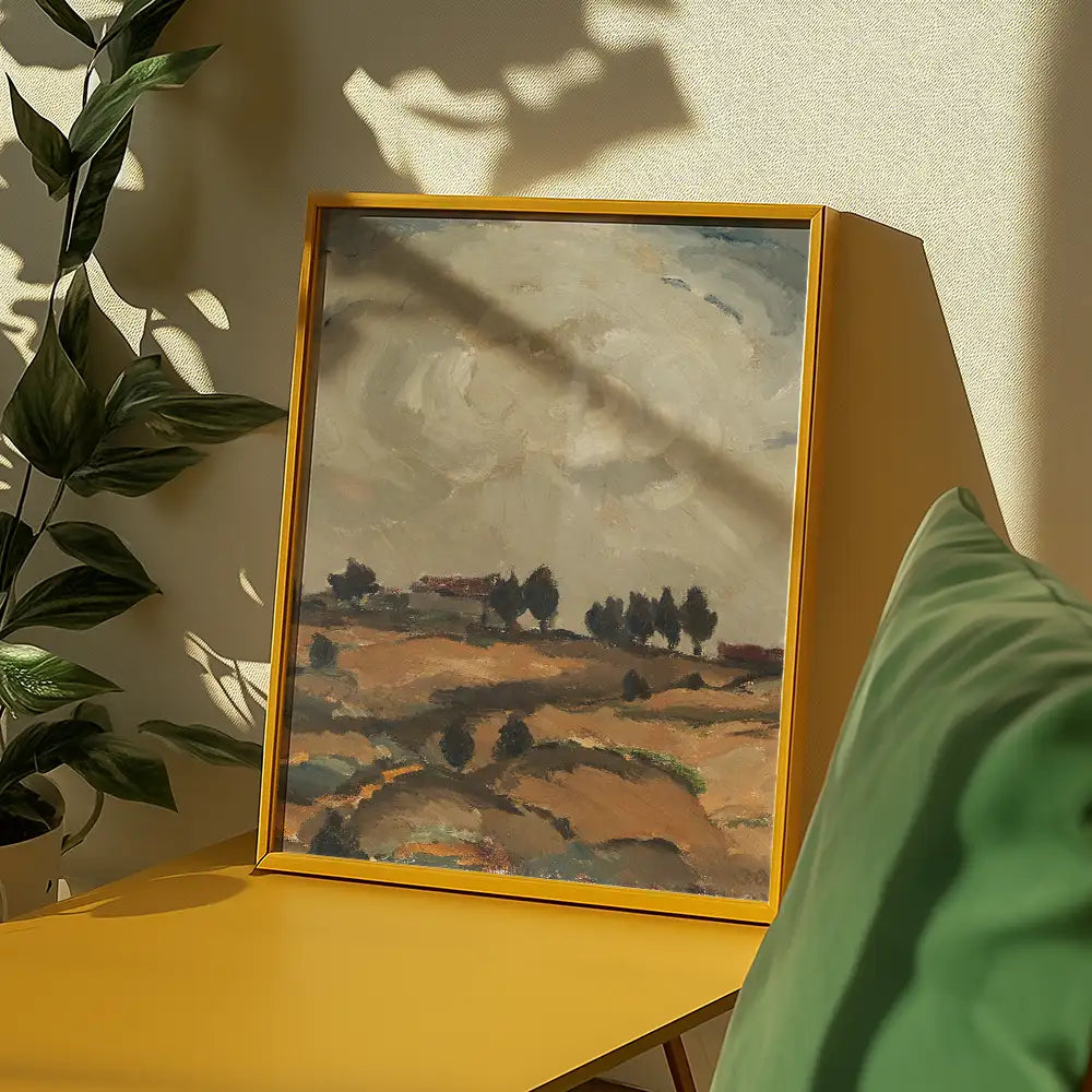 Framed landscape painting featuring hills, trees, and a cloudy sky, displayed on a yellow table with green cushions and a plant.