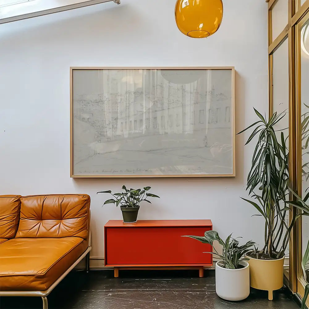 Framed abstract painting hanging on a wall, featuring a minimalist design, above a red cabinet in a modern living space with plants and a brown leather sofa.