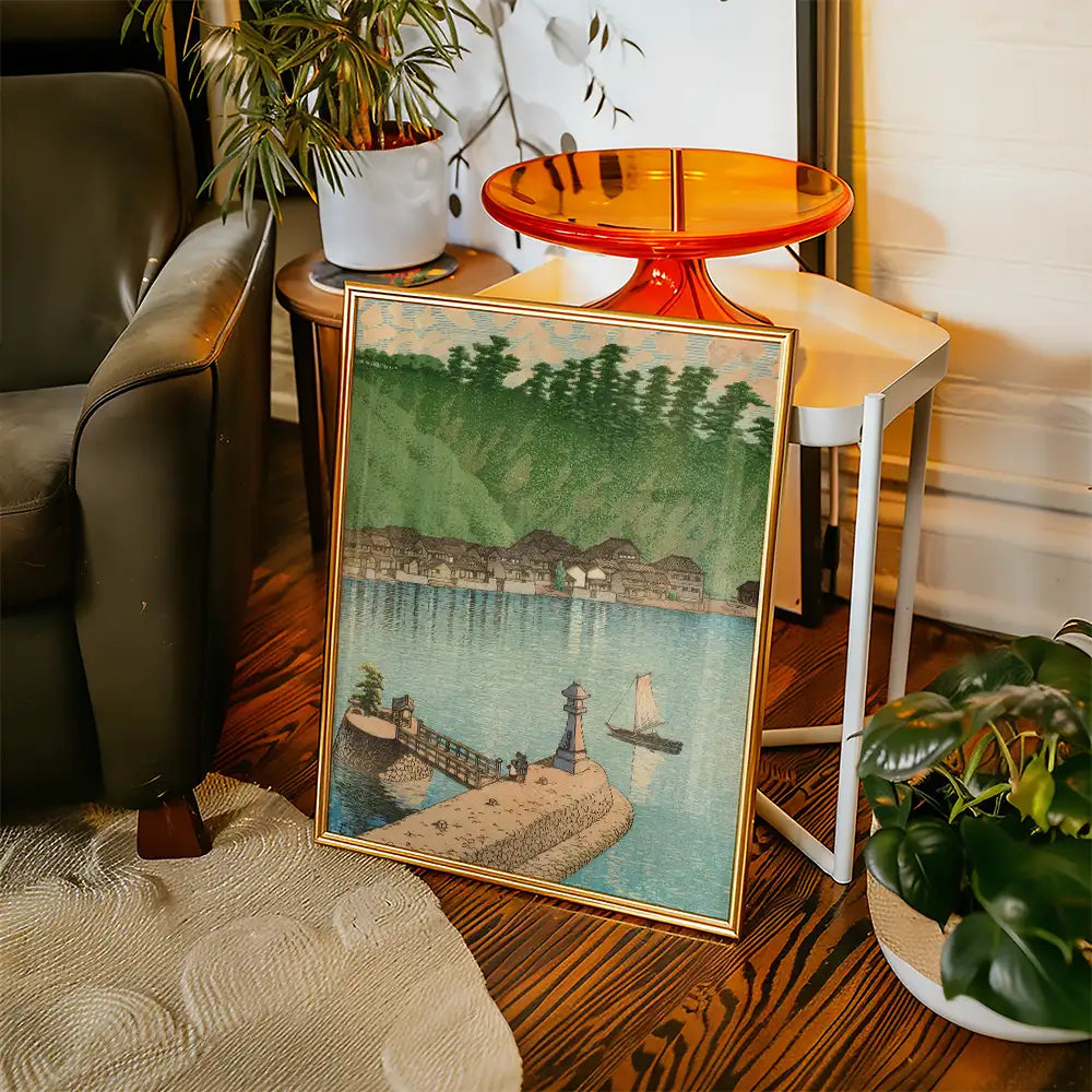 Framed painting of a serene waterfront scene with a lighthouse, boats, and distant houses, placed in a cozy living room setting.