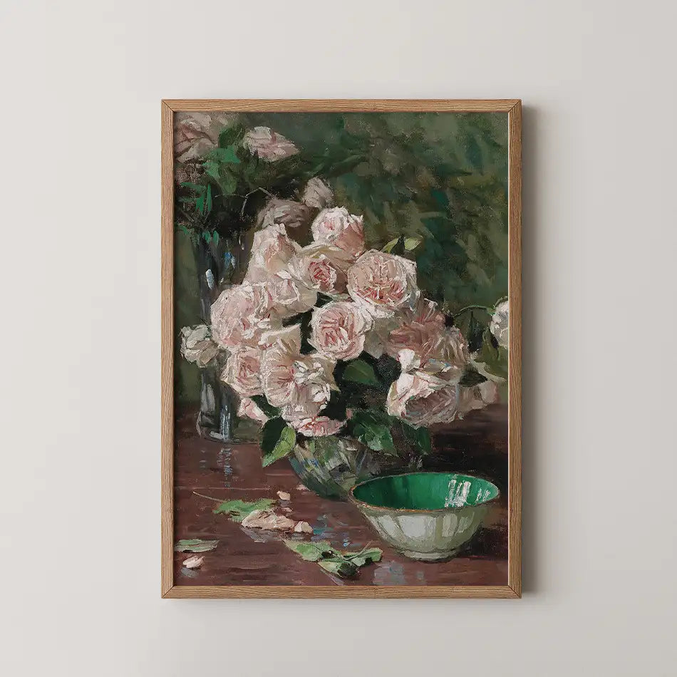 Framed painting of pink roses in a glass vase with a green bowl on a wooden table.