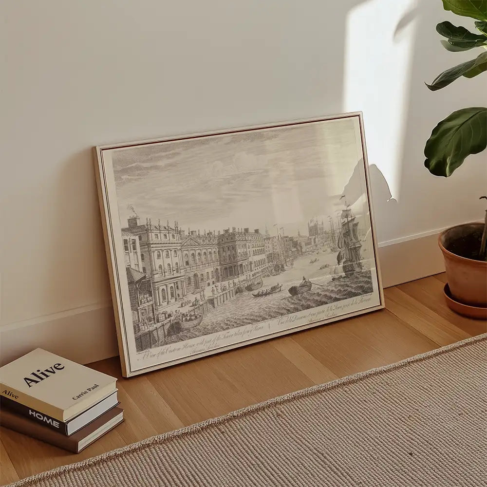 Framed vintage cityscape painting featuring boats along a river, leaning against a wall with a plant and books in the foreground.