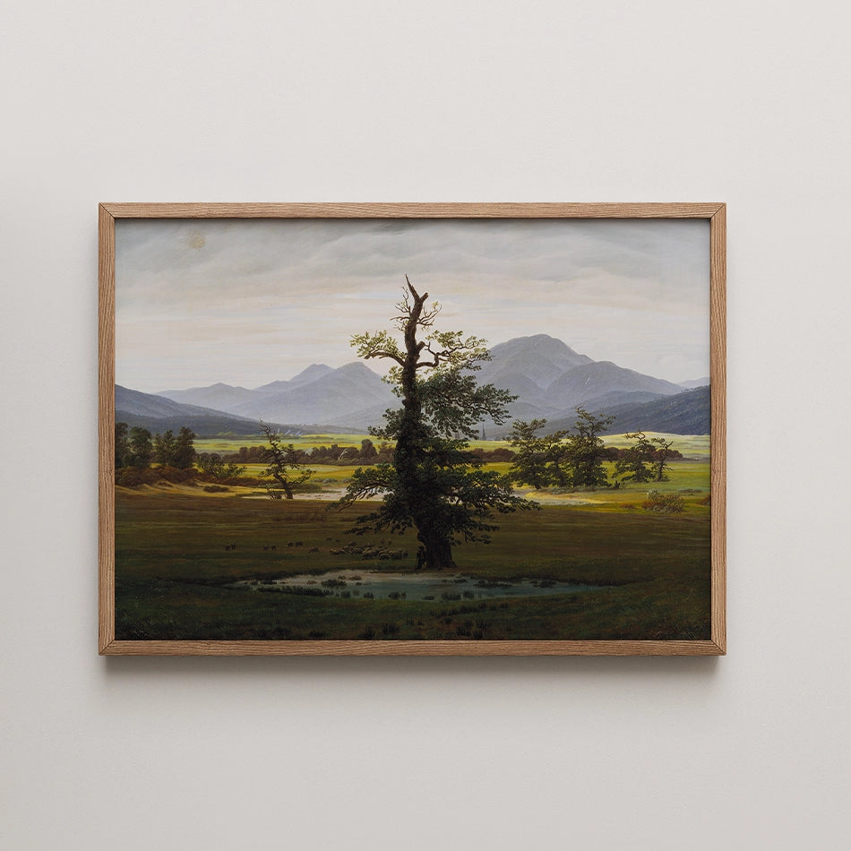 Landscape painting featuring a prominent tree in a meadow with mountains in the background, framed in wood.