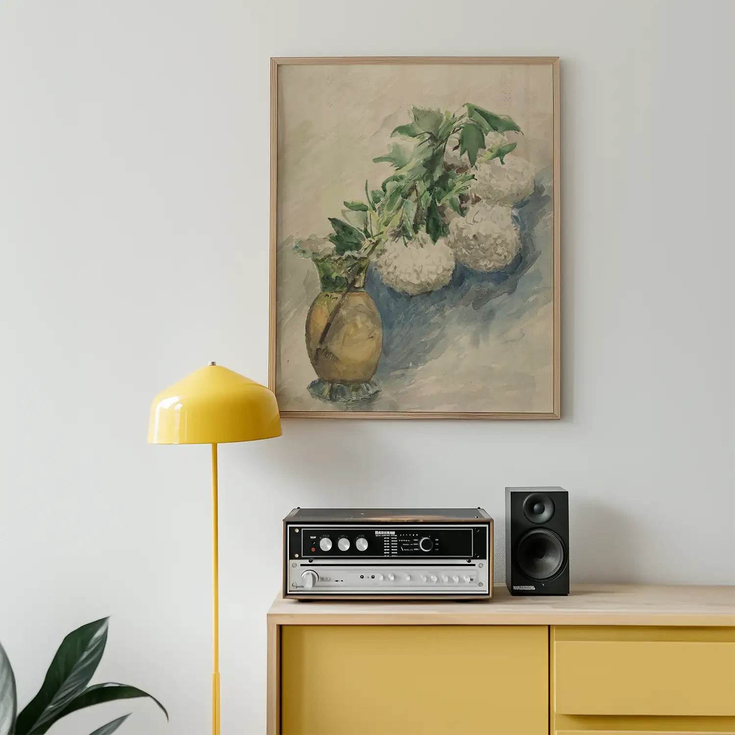 A framed painting of a vase with white flowers hanging on a wall above a retro record player and a yellow floor lamp in a modern interior setting.
