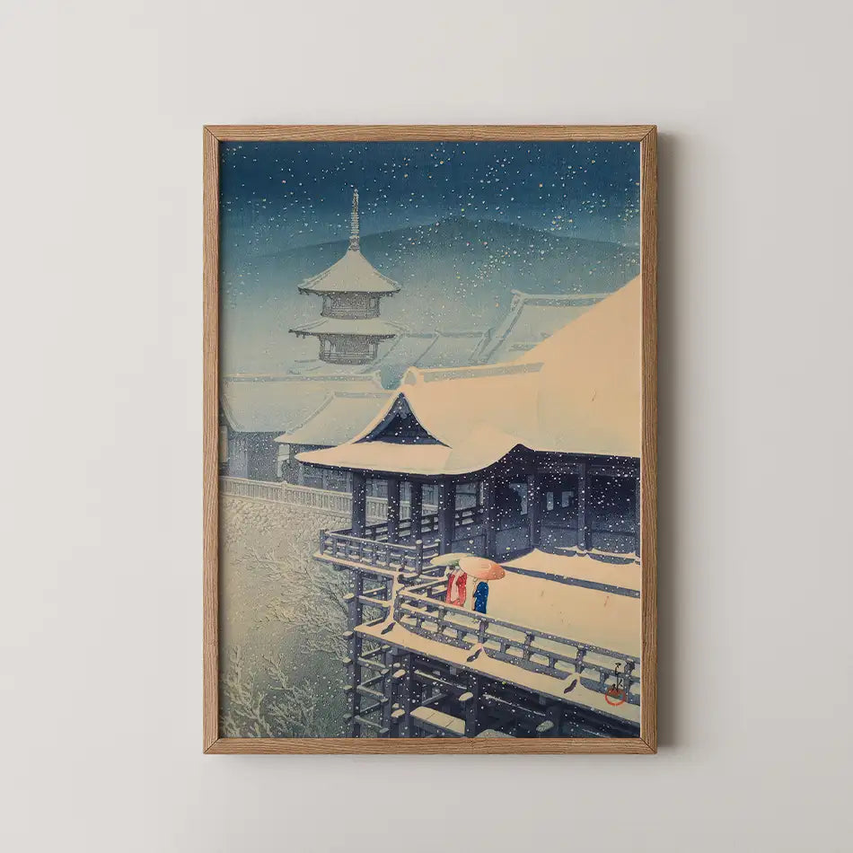 Painting of a snowy landscape featuring traditional Asian architecture and two figures under an umbrella, framed in wood.