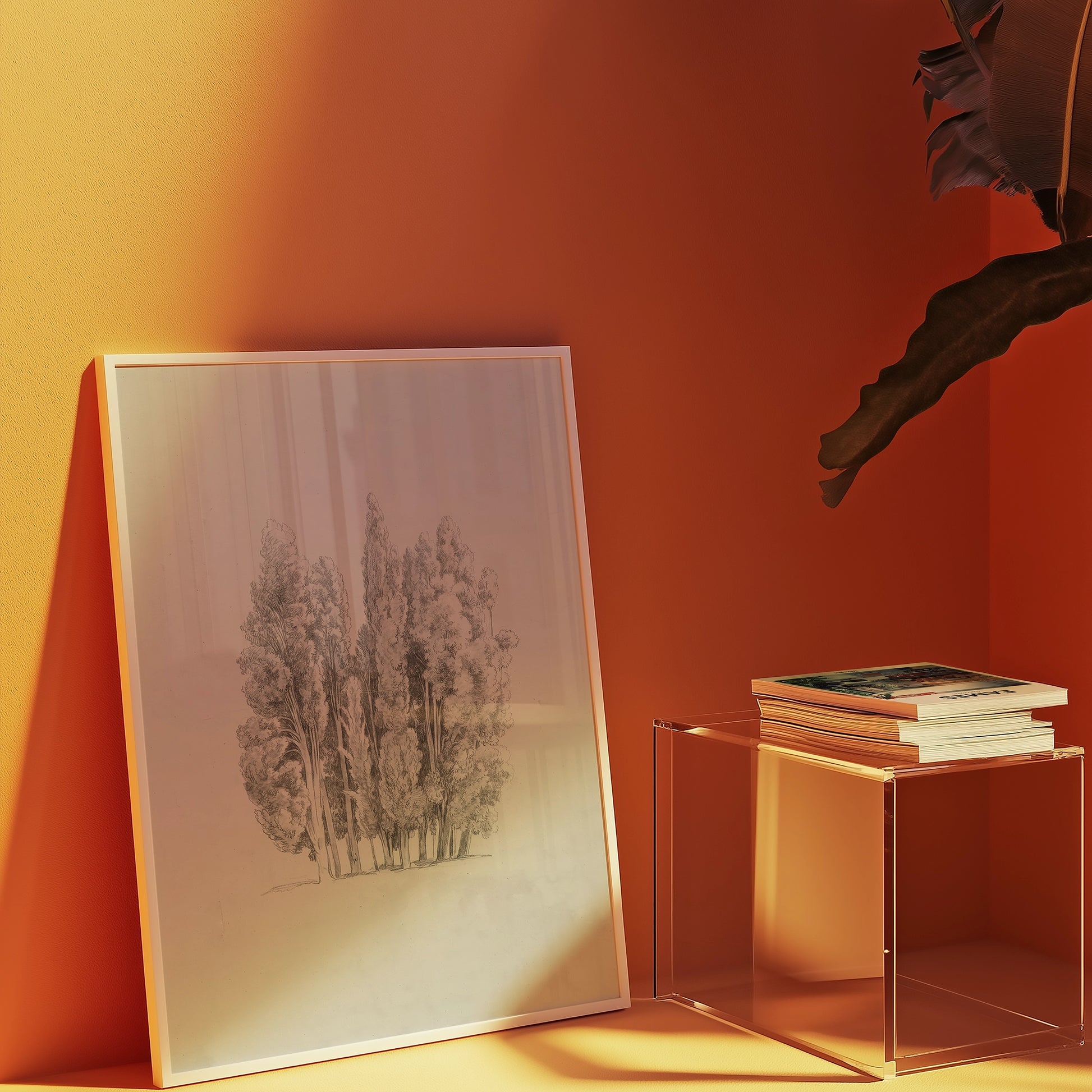 Framed black and white drawing of trees leaning against an orange wall, beside a glass side table with stacked books.