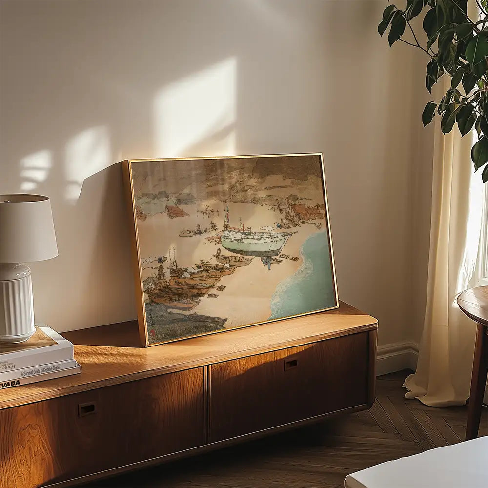 Framed painting of a coastal scene featuring boats on a sandy shore, displayed on a wooden console table in a bright room.