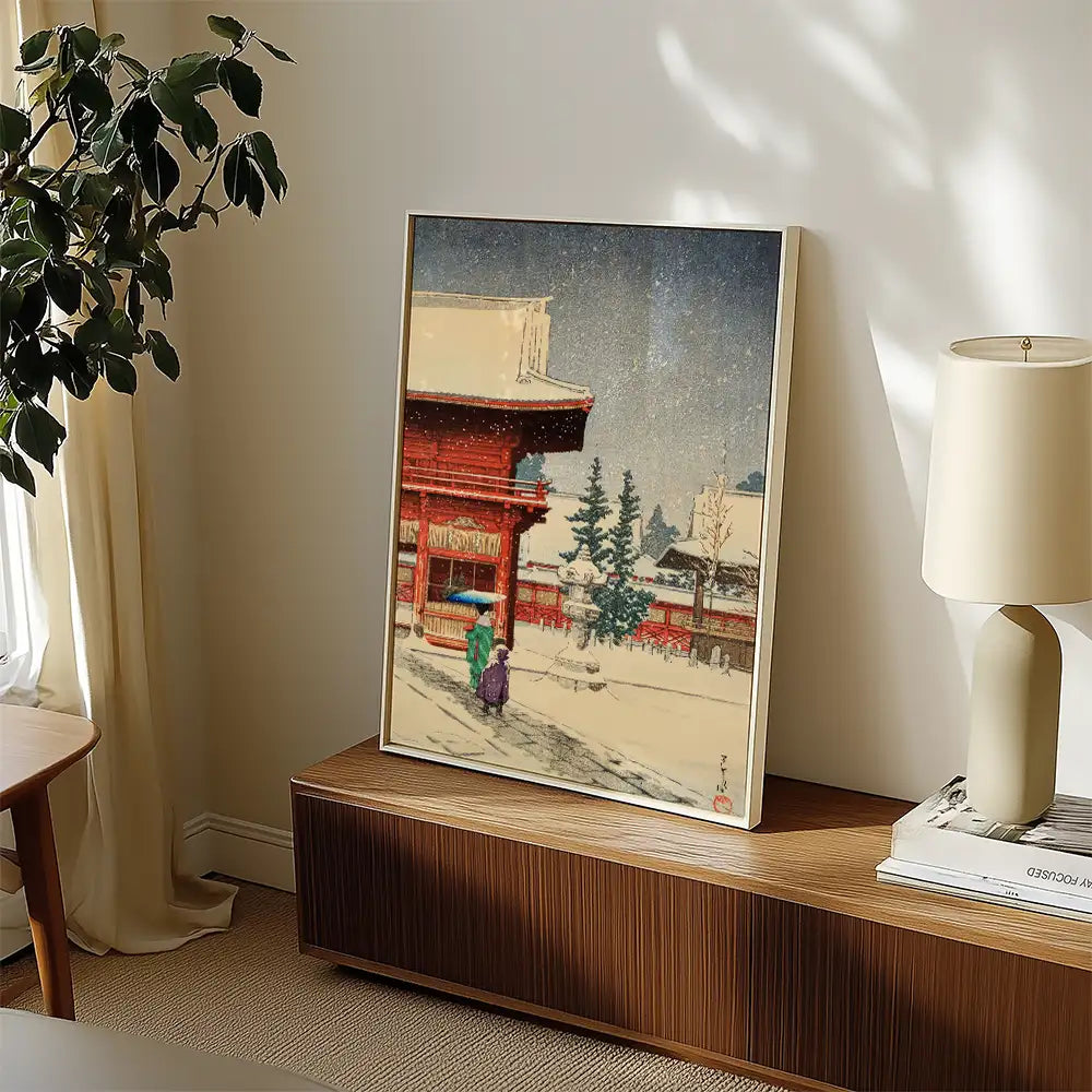 Painting of a snowy scene featuring traditional architecture and two figures walking, displayed in a stylish living room setting.