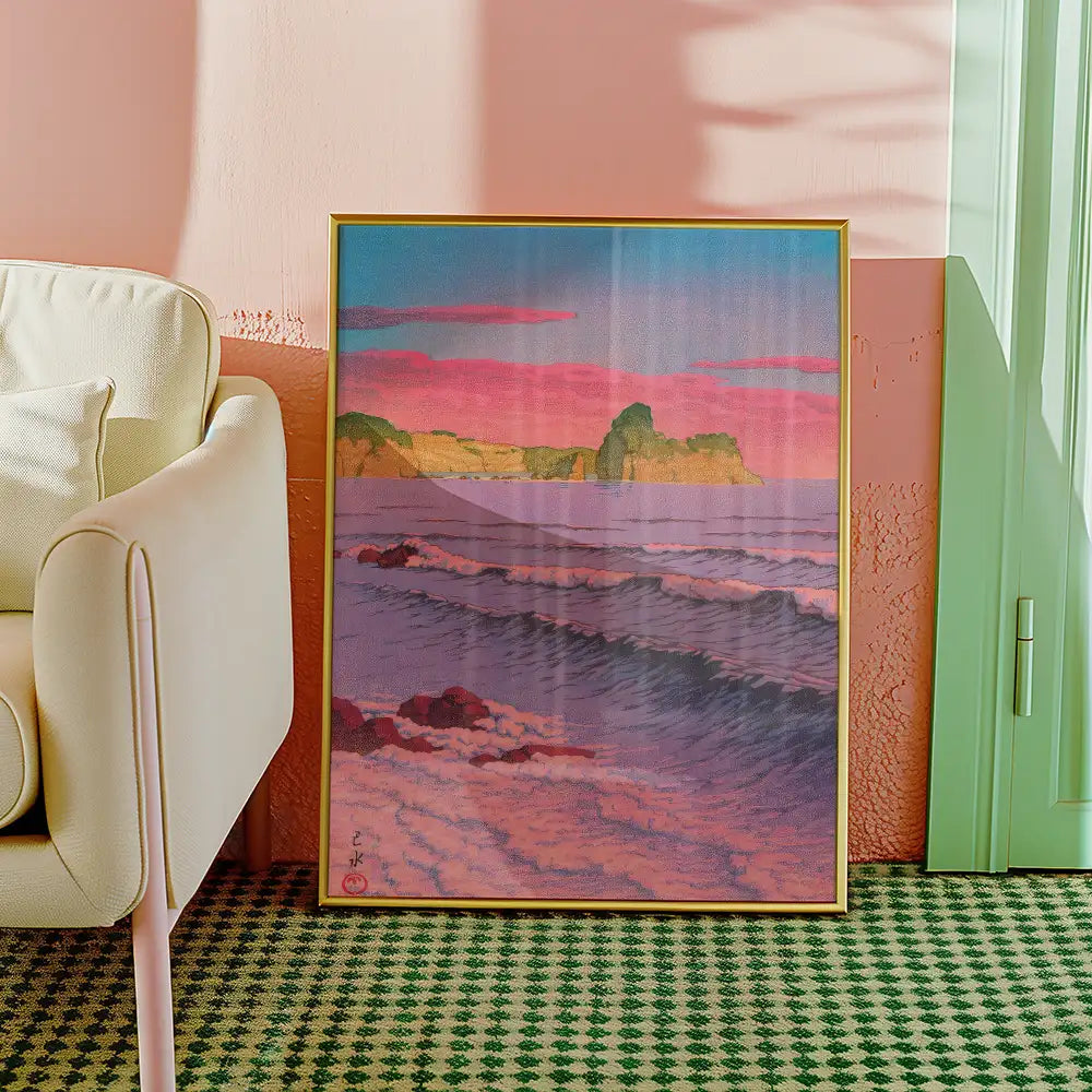 Framed painting of a serene ocean landscape at sunset, featuring waves and cliffs, placed next to a light-colored armchair in a stylish interior setting.