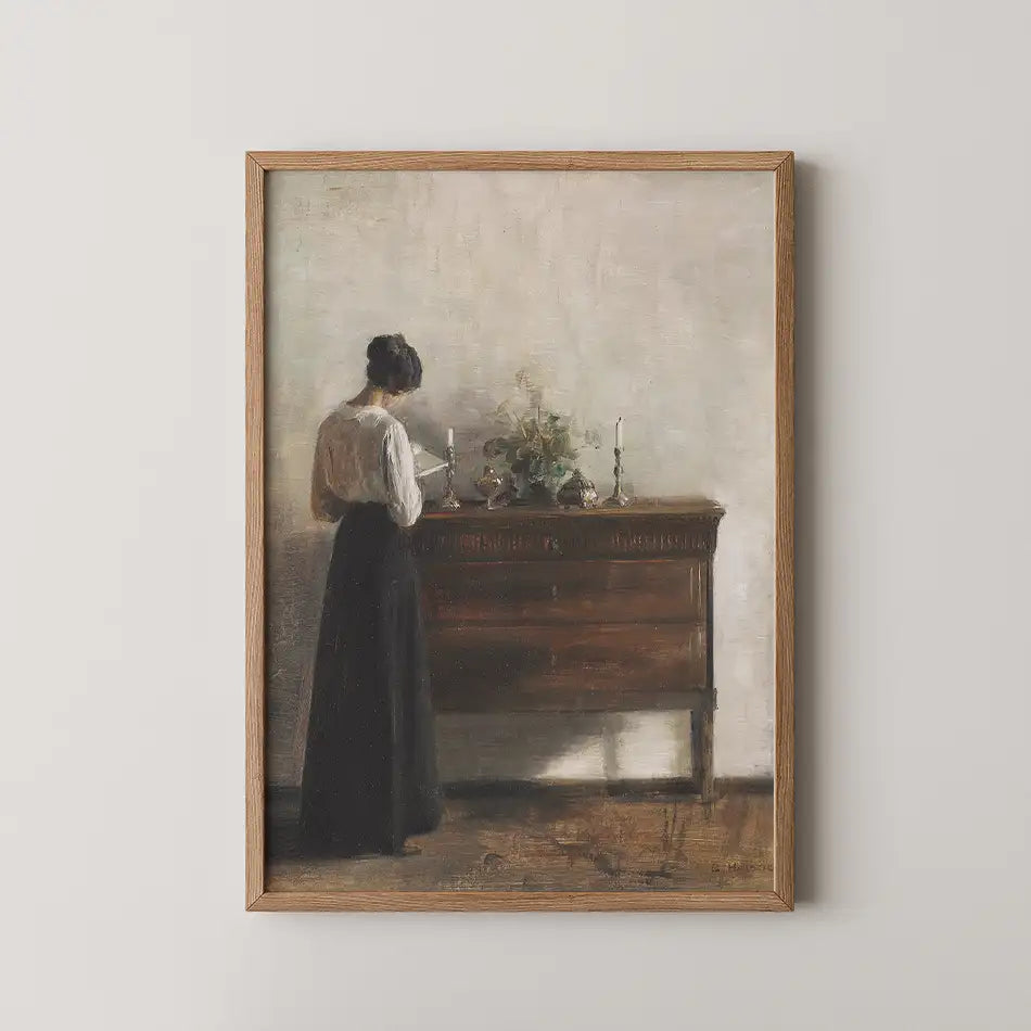 A woman in a black skirt and white blouse stands at a wooden side table adorned with candles and flowers, captured in a softly lit, impressionistic painting.