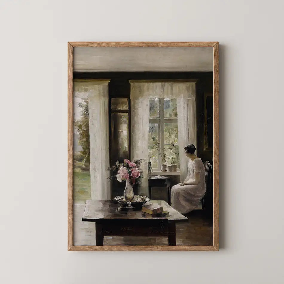 Painting of a woman sitting by a window in a softly lit room, with a table featuring a vase of pink flowers and books, framed in wood.