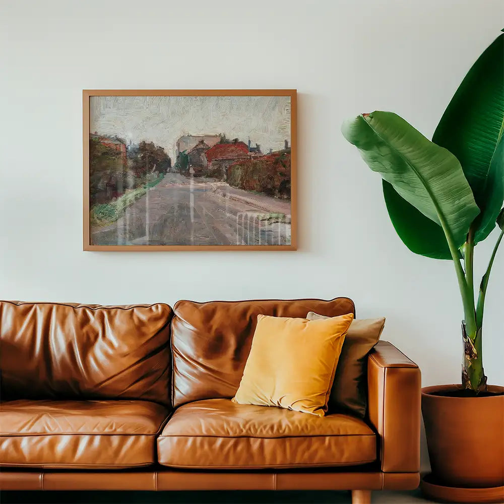 Framed painting of a serene rural scene hanging above a brown leather couch with a yellow cushion and a tall green plant in a pot.